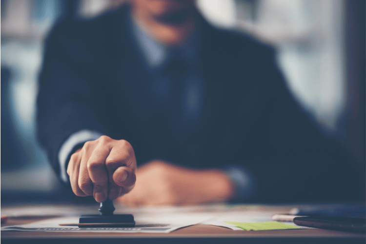 Close up of a person's hand stamping with approval a document on a desk